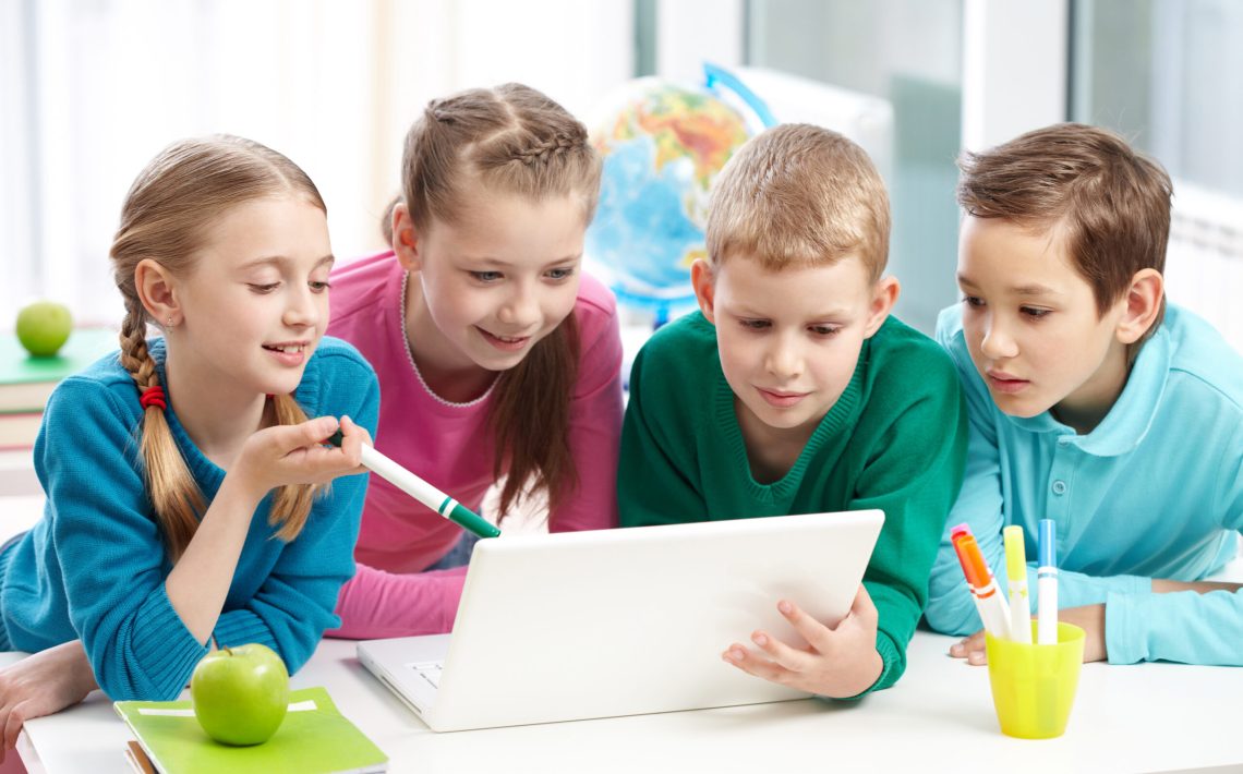 Portrait of smart schoolgirls and schoolboys looking at the laptop in classroom