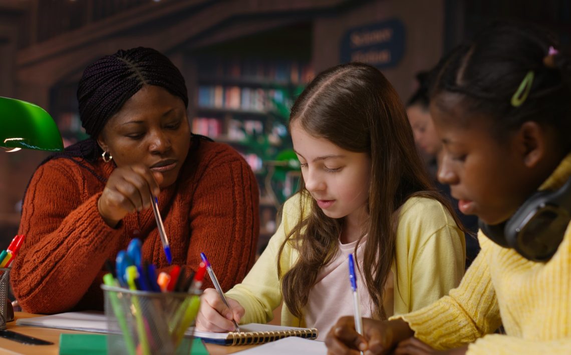 Female teacher assisting pupils with class homework and mentoring, providing academic instruction and support to help pass school assignments. Tutor lecturer gives private lessons. Camera B.
